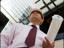 photo of business man in hard hat carrying blueprints